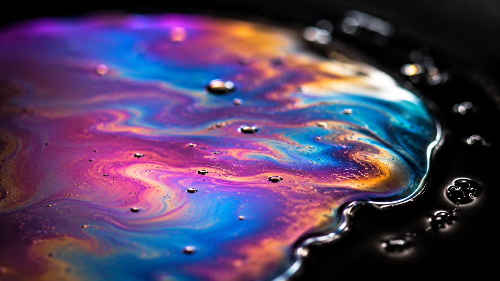 Iridescent oil-on-water macro — natural pink, violet, cyan and gold rainbow gradients in surface tension