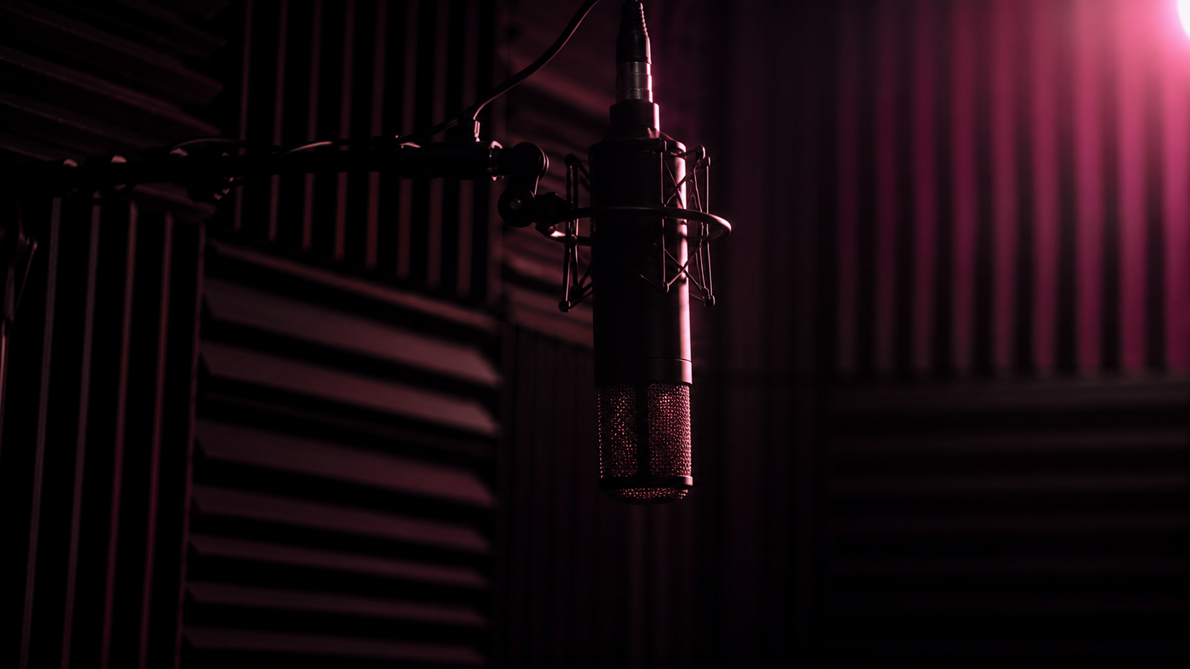 AUVIO vocal booth at night — condenser mic on suspended boom arm, foam acoustic panels, soft pink rim light